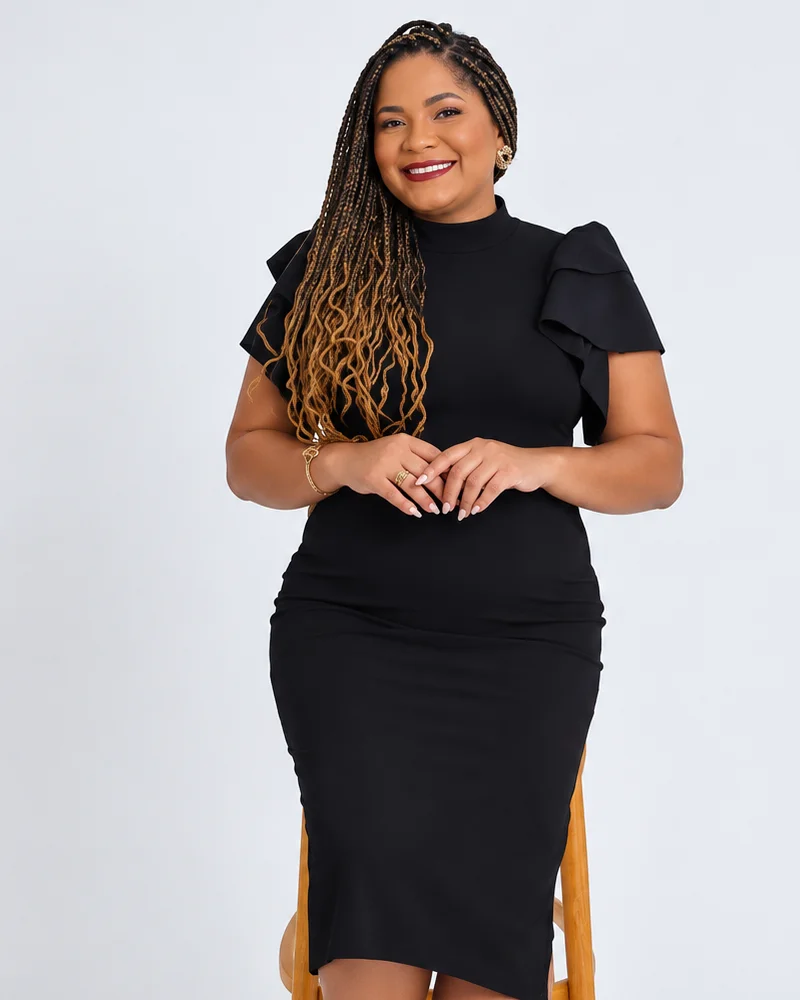 Dra. Vanessa Costa sorrindo, de vestido preto, sentada em um banco de madeira